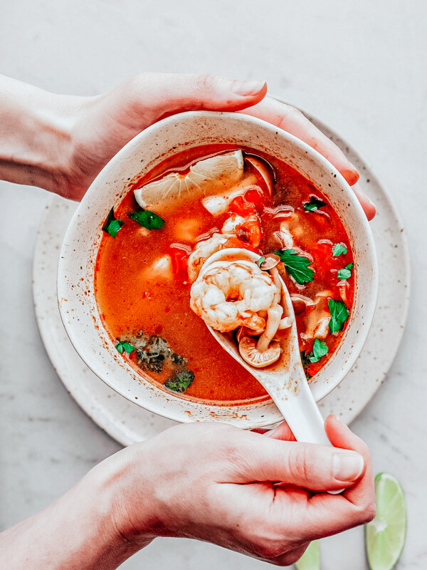 Bowl of Tom Yum Soup with hand spooning up shrimp.