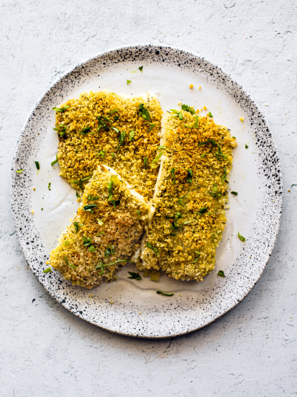 Crispy golden baked flounder on a white speckled serving plate, garnished with fresh parsley.