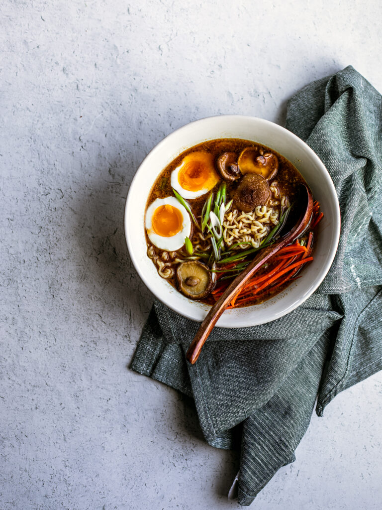 Off center shot of bowl of miso ramen with blue dish towel folded around it.