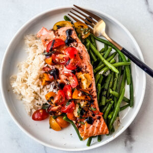 Fillet of salmon with bruschetta topping on a plate with rice and green beans.