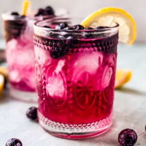 Blueberry vodka club soda in glass with lemon wedge.