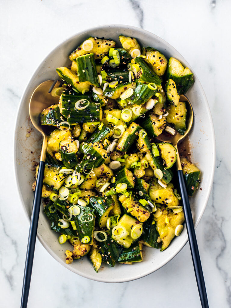 White serving bowl of smashed cucumber salad.