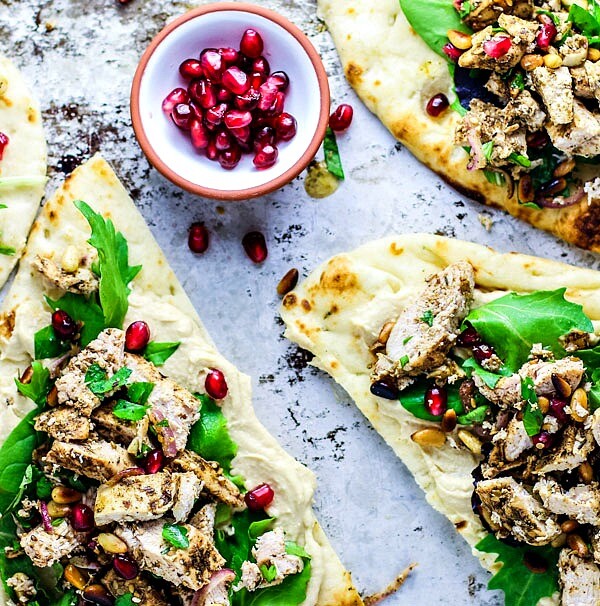 Naan breads topped with hummus, chicken, and greens.