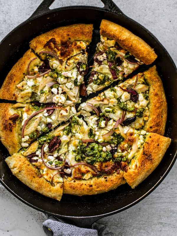 Skillet with chicken pesto pizza cut into slices.