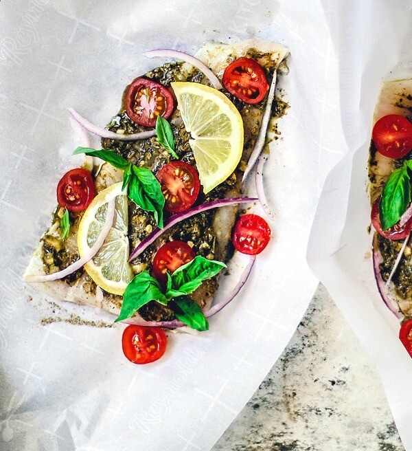 Flounder fillets sitting on parchment paper topped with bright ingredients.