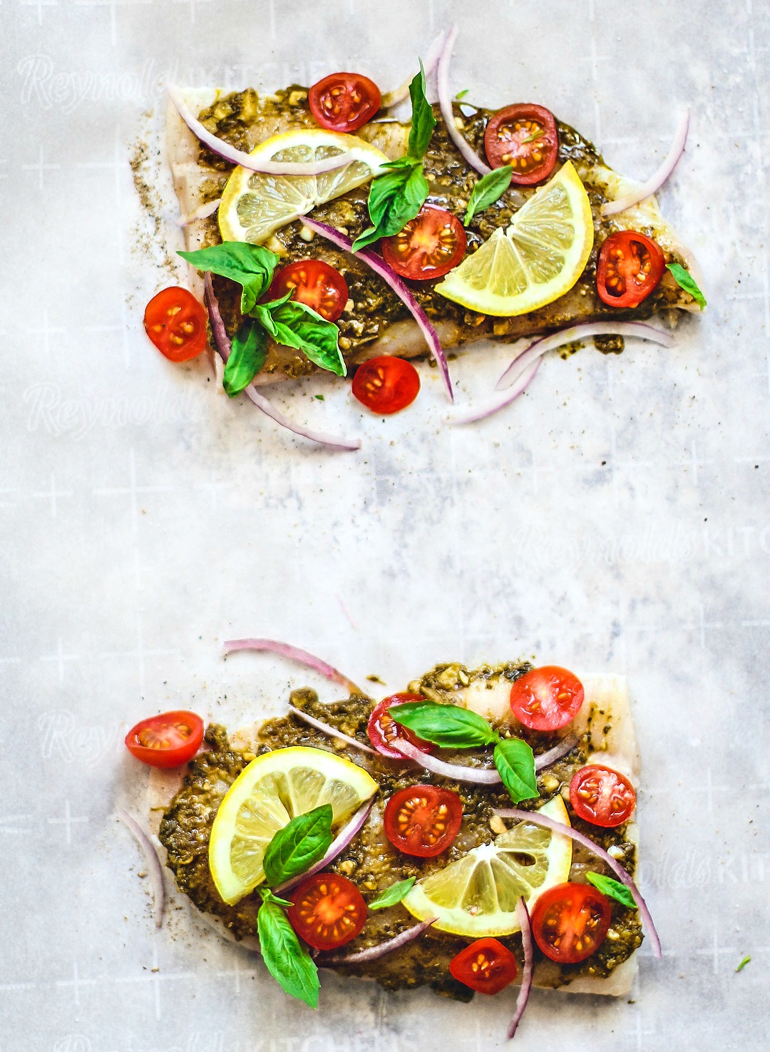 Flounder fillets sitting on parchment paper topped with bright ingredients.