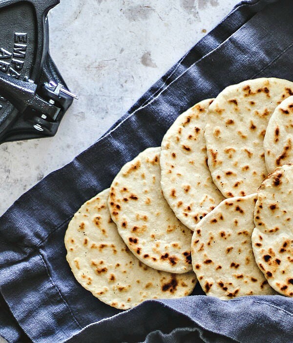 Homemade flour tortillas sprawled out on towel next to tortilla press.