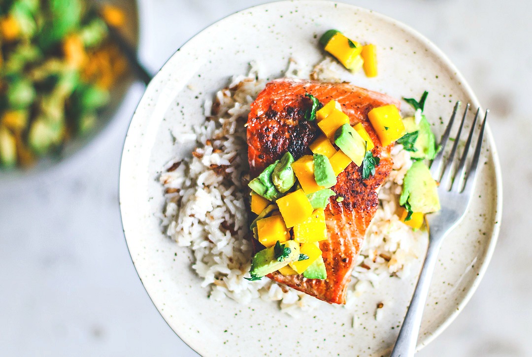 Pan-Seared Salmon on plate over rice and topped with mango and avocado salsa.