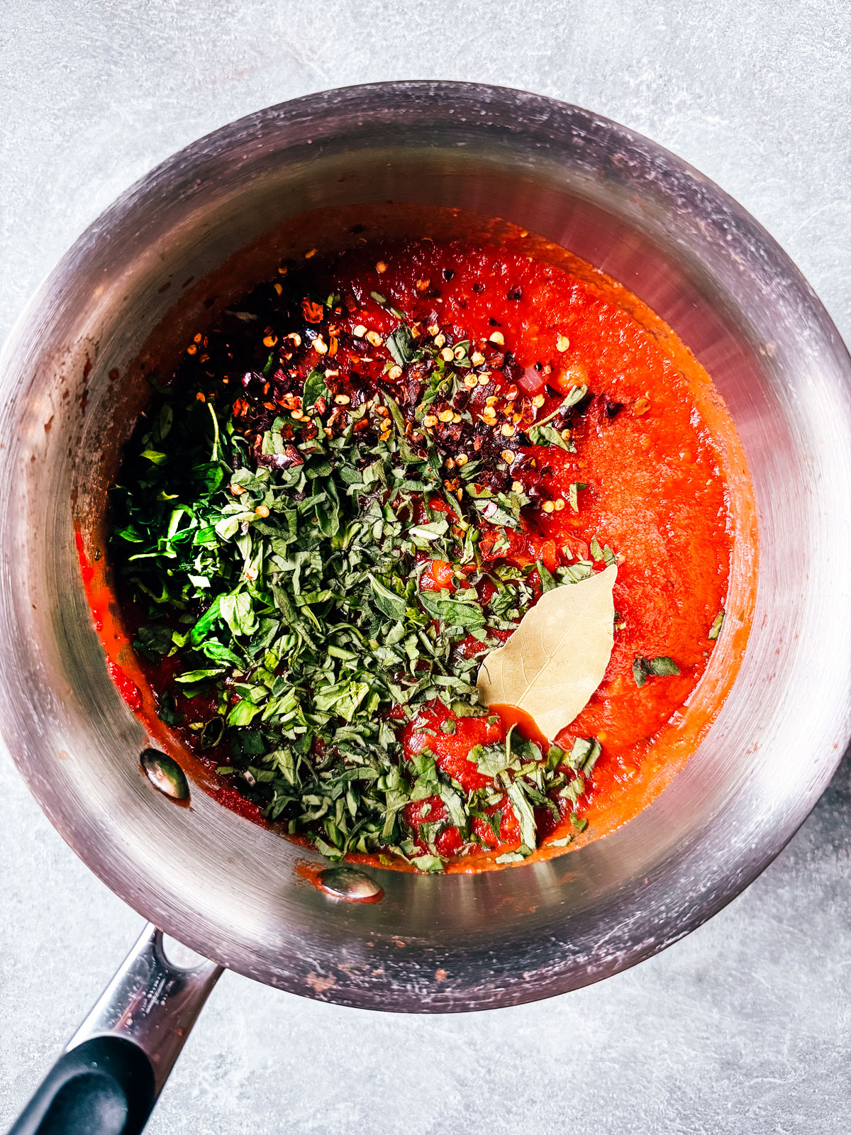 Crushed tomatoes and herbs in saucepan.