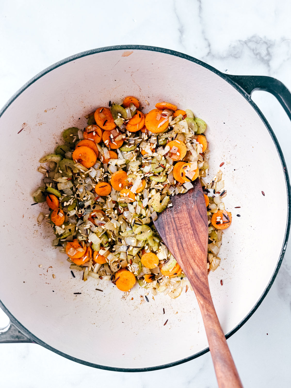 Wild rice mixed with celery, carrots and onion in pot.