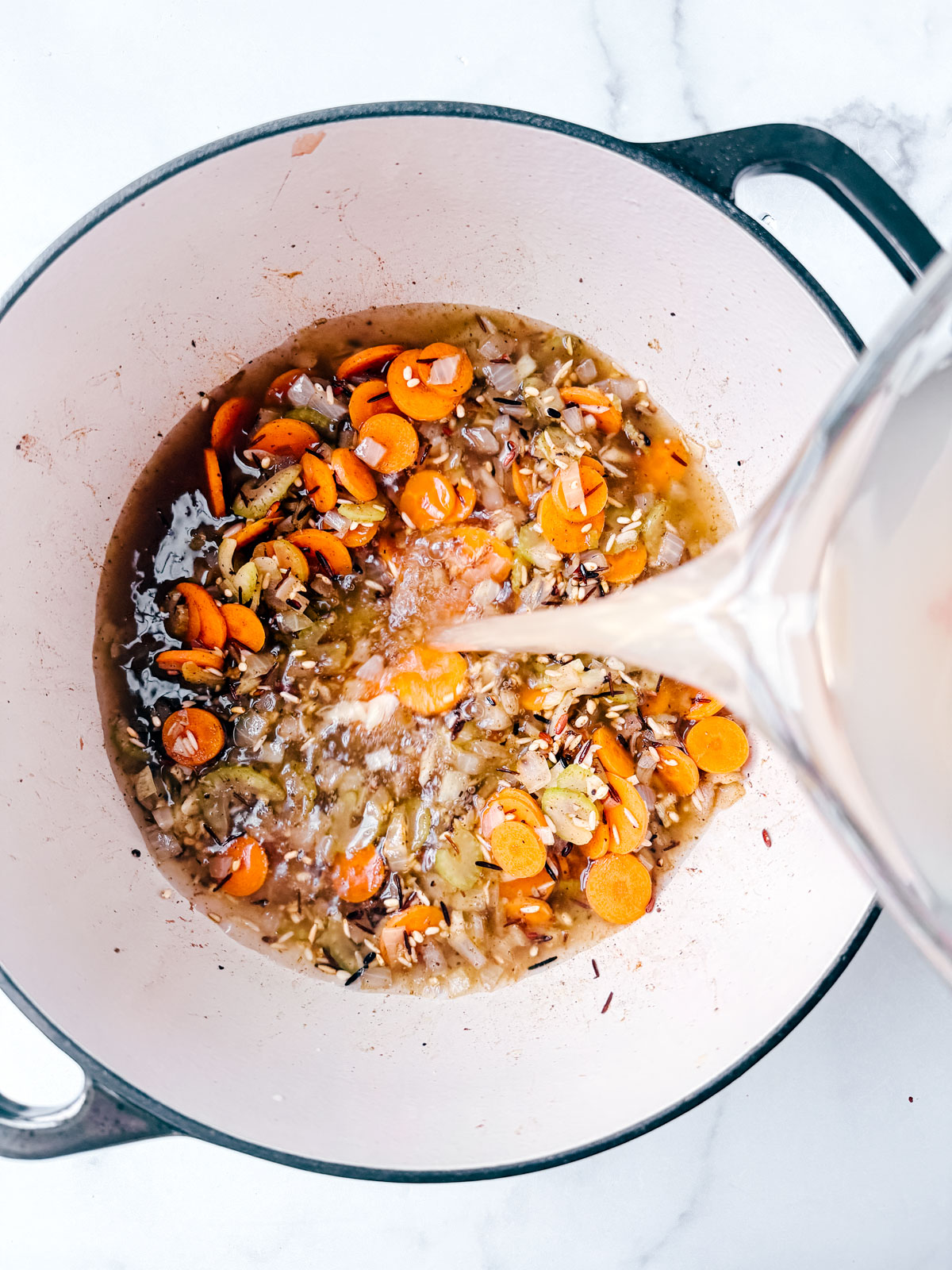 Turkey broth being poured into the pot with the rice and veggies,