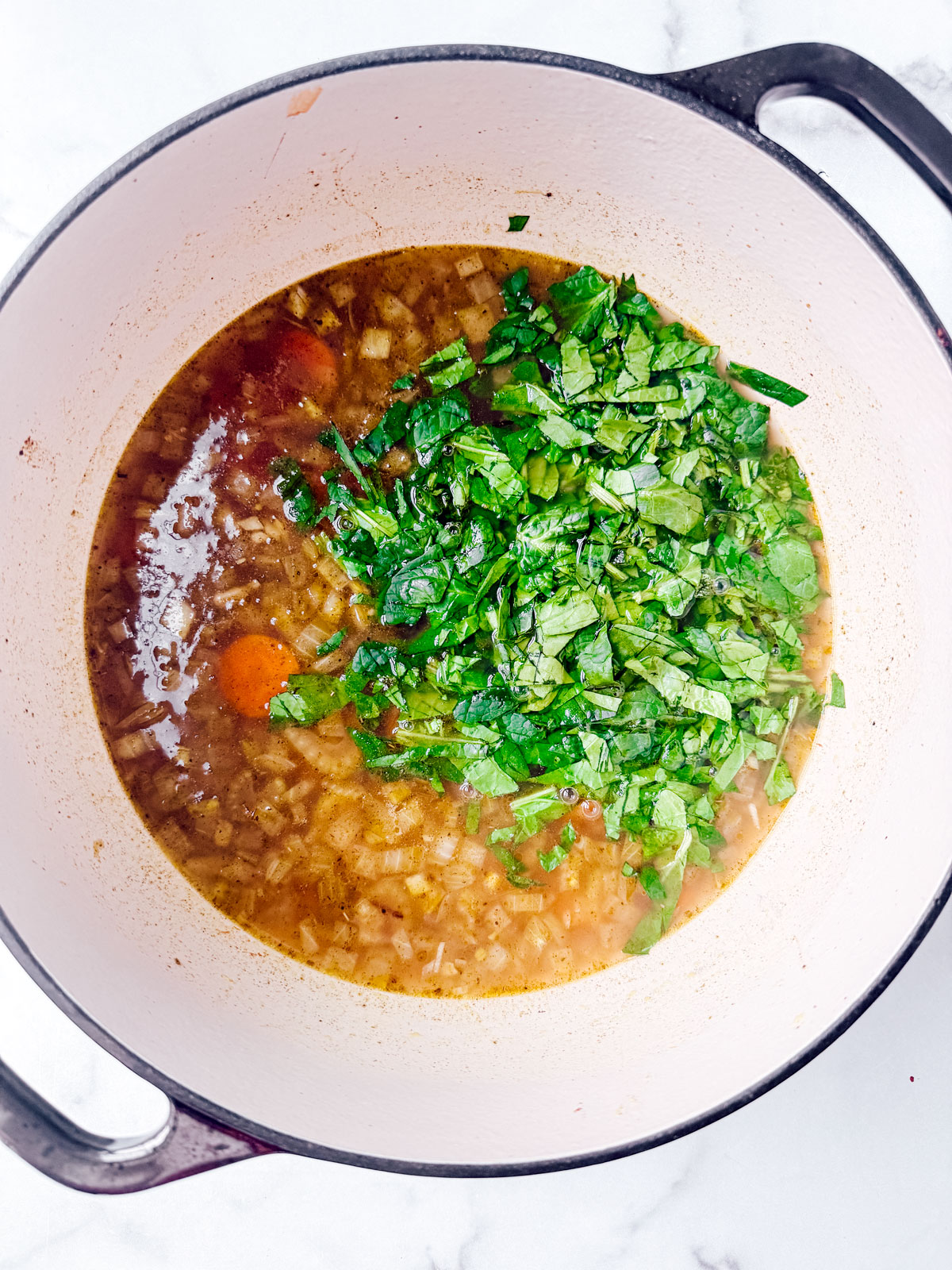 Baby spinach added to the soup in a large pot.