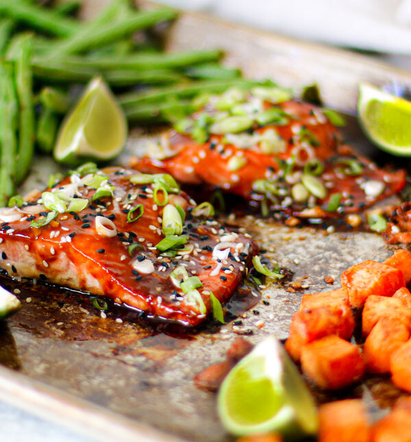 Two fillets of salmon on a sheet pan with veggies.