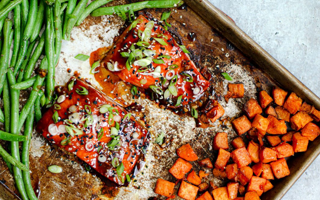 Two fillets of salmon on a sheet pan with veggies.