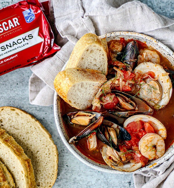 Bowl of cioppino with fresh bread and King Oscar Kipper Snacks packaging.