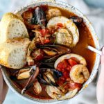 Hands holding bowl of cioppino.