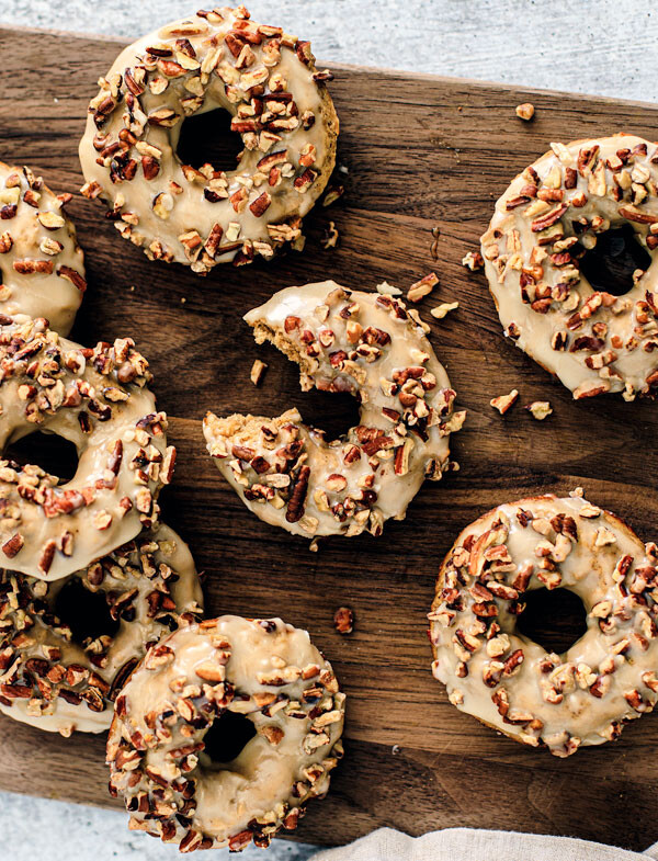 Wooden board full of maple baked donuts with pecans on top.