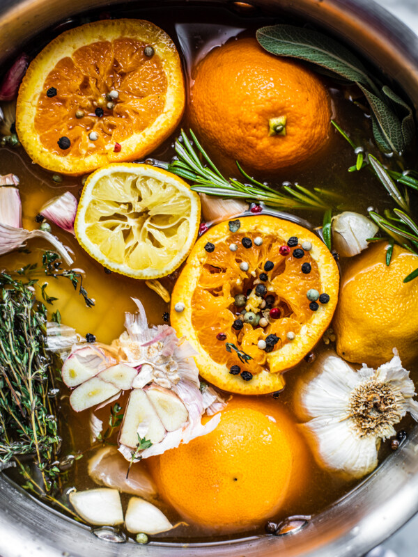 Large stock pot full of fresh herbs, oranges, lemons, peppercorns, and garlic.