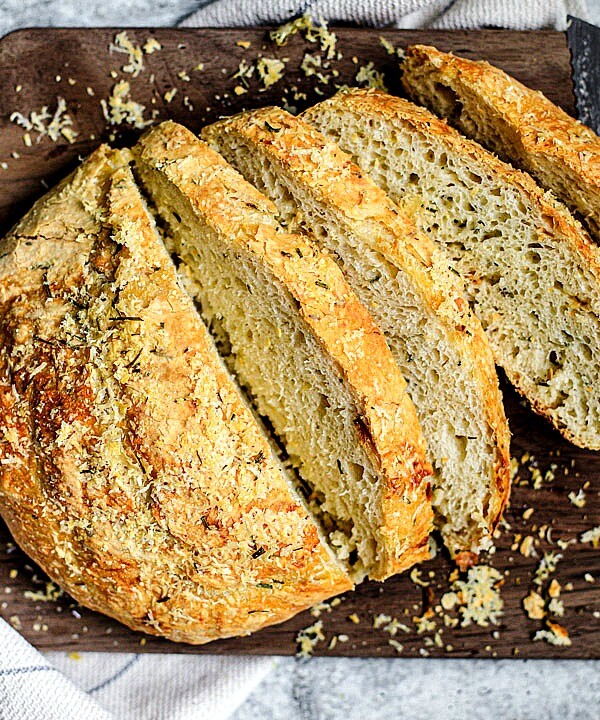 Sliced loaf of homemade bread with roasted garlic and rosemary, sliced on a cutting board.