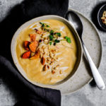 Bowl of roasted garlic and parsnip soup garnished with toasted pine nuts, root chips, and microgreens.