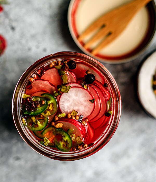 Close up of jar of pickled radishes with spices in the background.