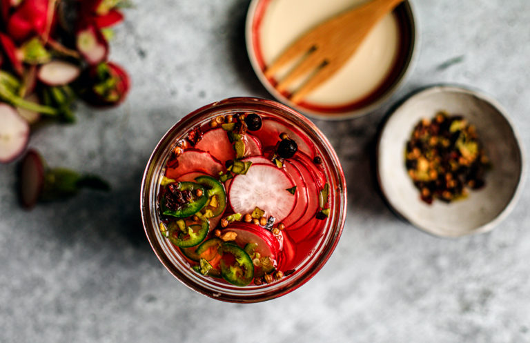 Close up of jar of pickled radishes with spices in the background.