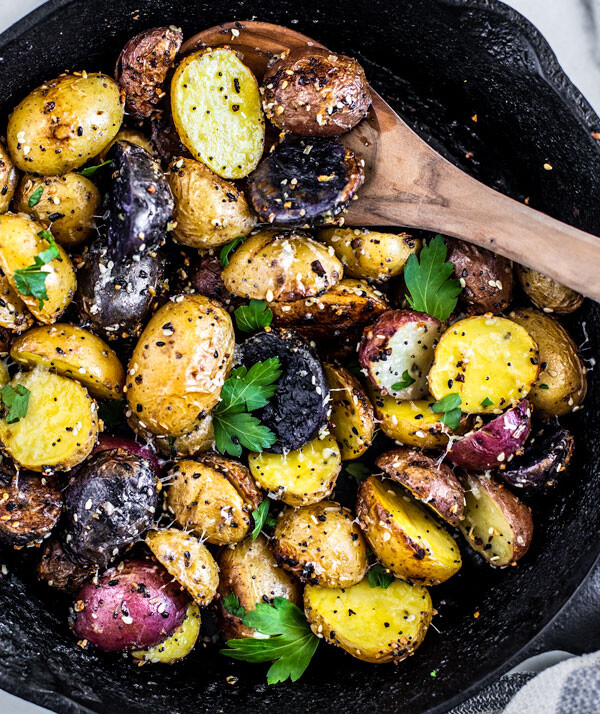 Cast iron skillet full of everything bagel seasoned roasted potatoes with fresh herbs on top.