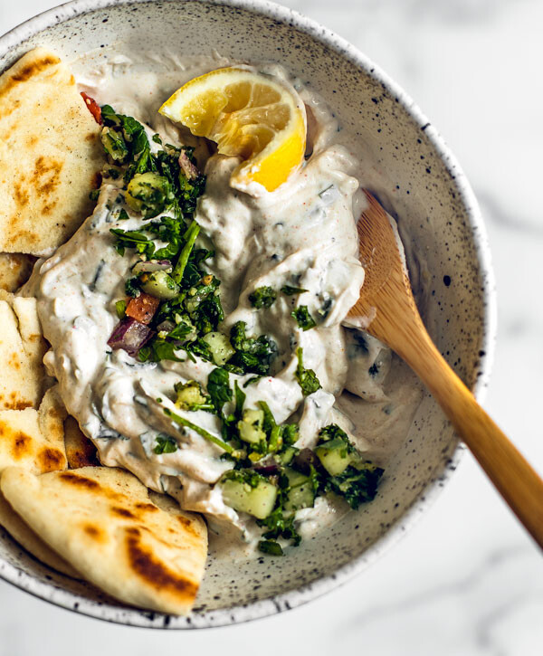 Bowl of mint Greek yogurt sauce with pitas and a squeezed lemon.