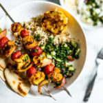 Plate of rice, tabbouleh, and pitas with grilled Moroccan chicken skewers on top.