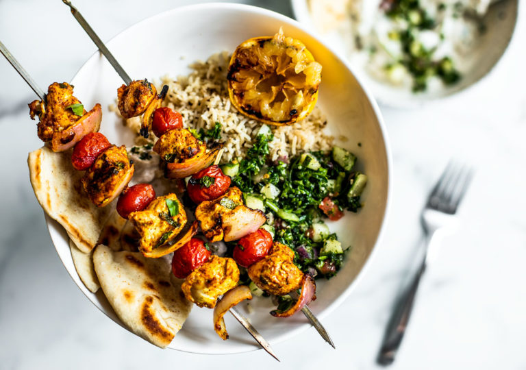 Plate of rice, tabbouleh, and pitas with grilled Moroccan chicken skewers on top.