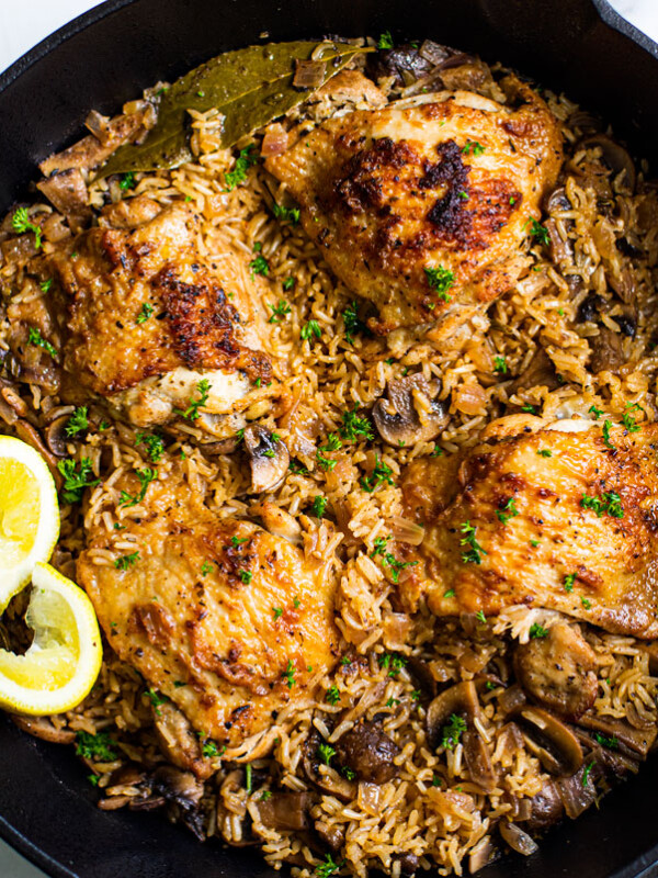 Close up of pan full of cooked rice, mushrooms, golden crisp chicken thighs, and lemon wedges.
