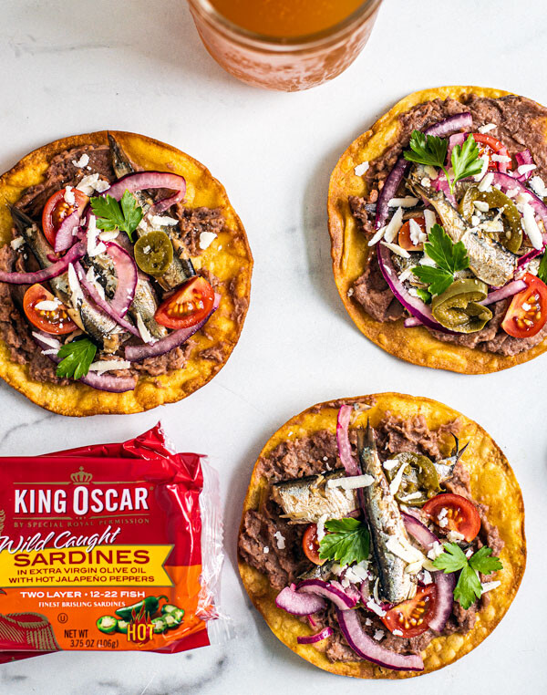 Spicy tostadas laid out around pints of beer and cans of King Oscar sardines.
