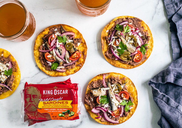 Spicy tostadas laid out around pints of beer and cans of King Oscar sardines.