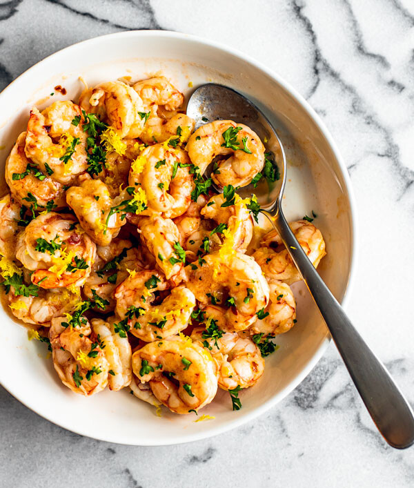 White serving bowl full of buttery shrimp garnished with fresh parsley.