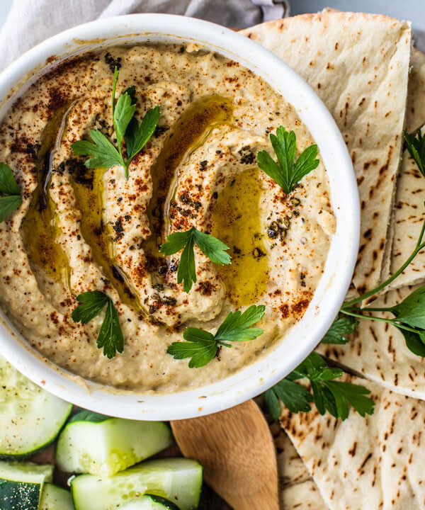 Close up of homemade baba ganoush in bowl with platter of pita and cucumbers.