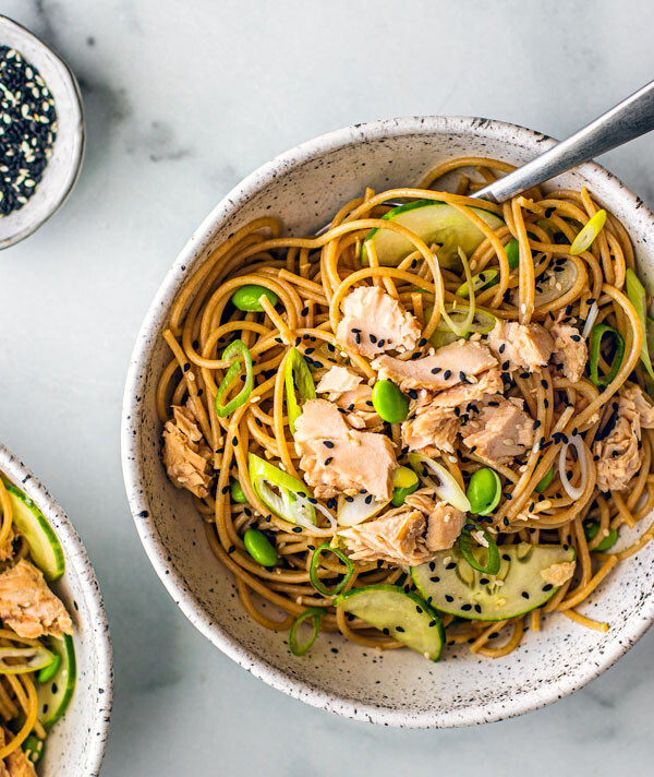 Soba noodles in a bowl with salmon, edamame, cucumbers, and scallions.