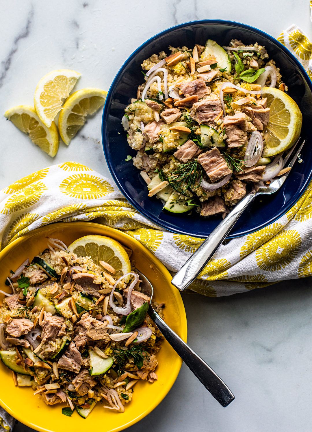 Two bowls of quinoa topped with large flakes of tuna and lemon wedges.