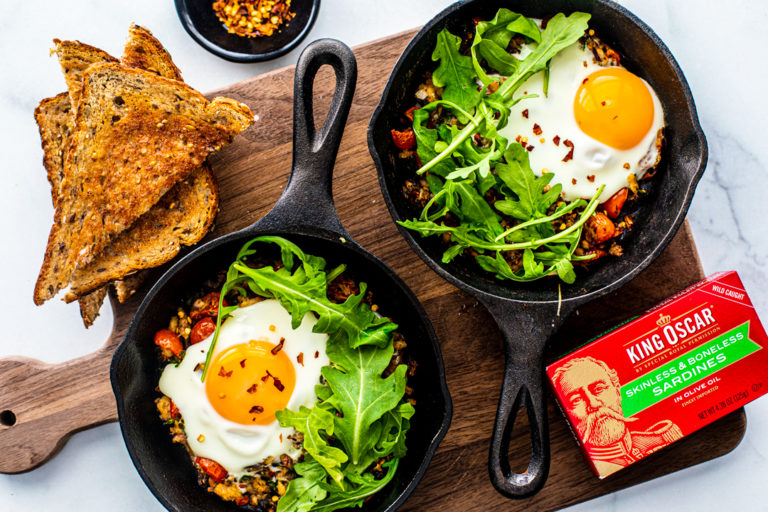 Two miniature skillets filled with Fisherman's Eggs and topped with arugula.