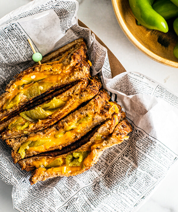 Hatch chile grilled cheese in newspaper next to a bowl of fresh Hatch chiles.