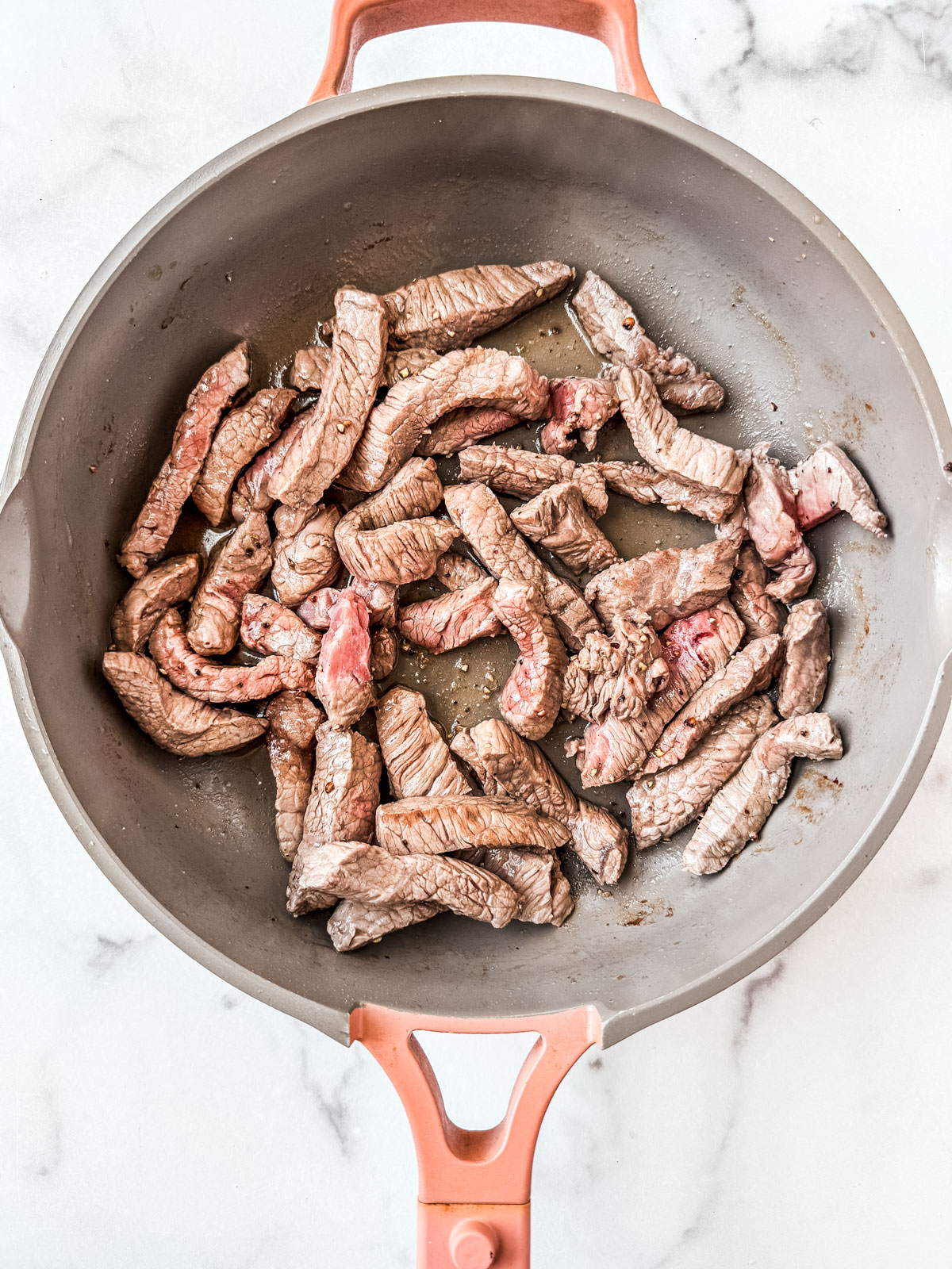 Beef strips being cooked in a skillet.