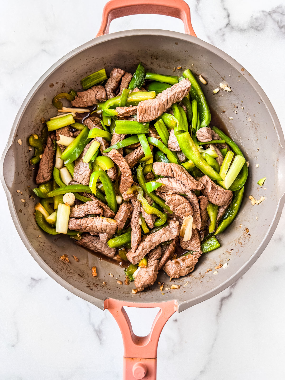 Beef, peppers, and scallions in a skillet.