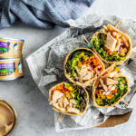 Overhead shot of wraps with jar of hummus and cans of Genova tuna.