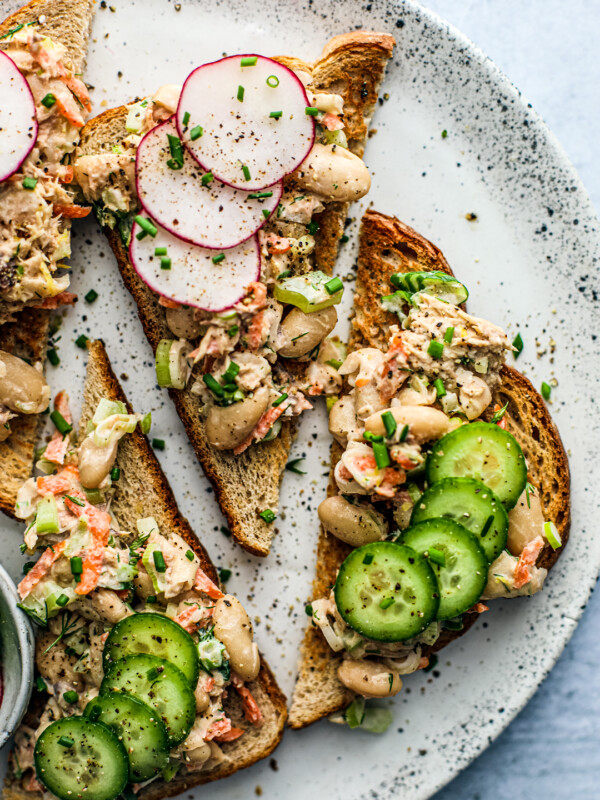 Overhead close up of fancy toasts topped with mackerel and white bean salad, radishes, and cucumbers.