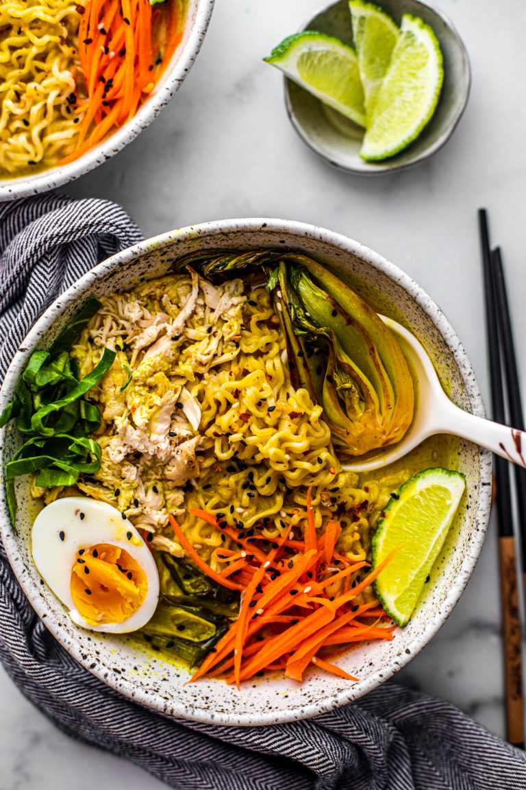 Overhead shot of bowl of chicken curry ramen soup with side of limes.