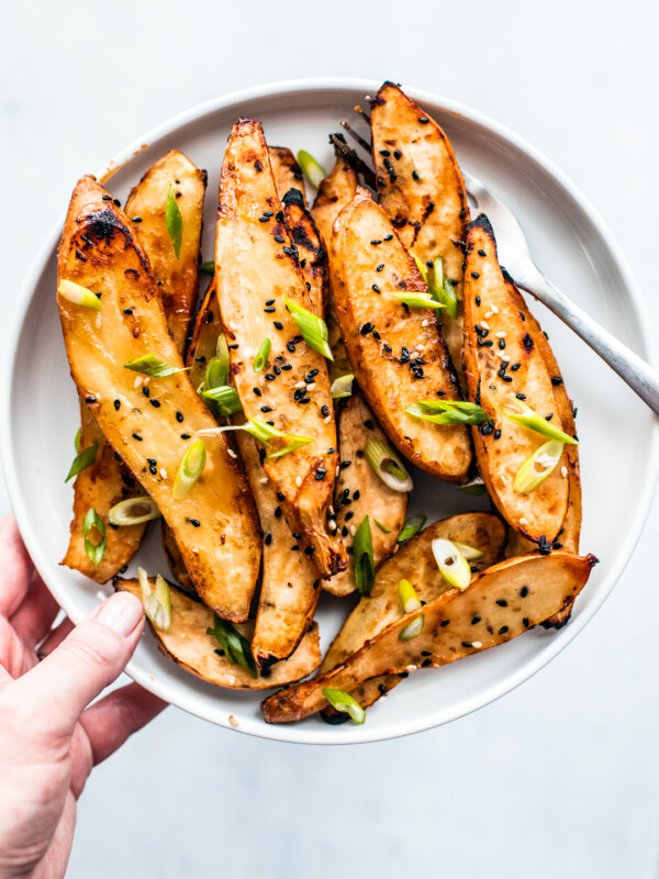 Overhead shot of hand holding up plate of honey miso roasted sweet potatoes garnished with scallions.