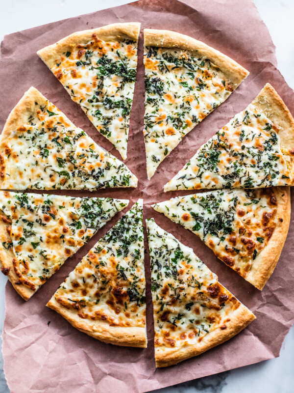 Overhead shot of cooked herb and garlic cheese pizza cut into slices on parchment paper.