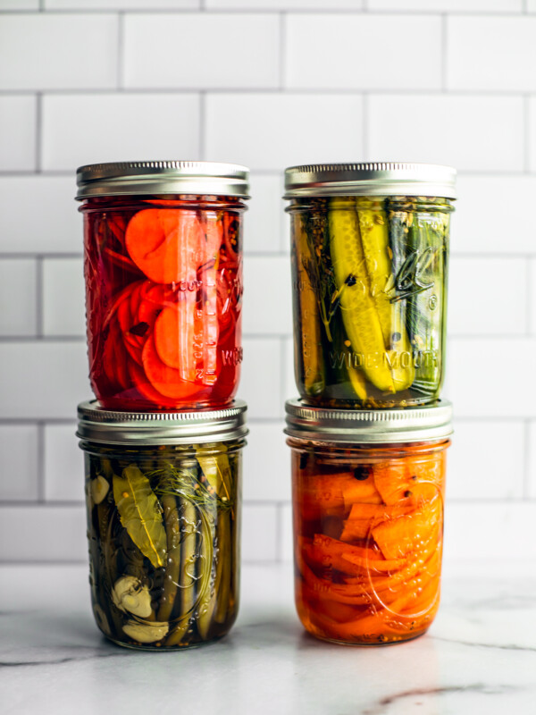 Four colorful jars of quick pickled vegetables stacked on top of on another.