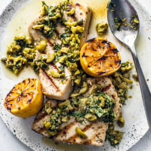 Overhead shot of grilled swordfish steaks on a plate smothered in olive and herb sauce.