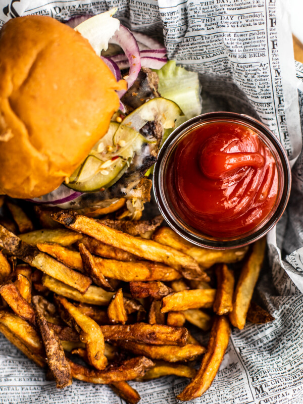 Homemade ketchup in small jar on platter with burger and fries.