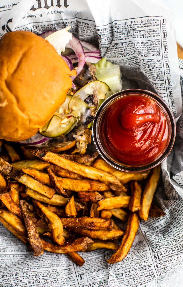 Homemade ketchup in small jar on platter with burger and fries.